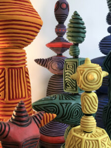 Group of bright orange, yellow, green hit, pink purple of hand-built clay sculptures with horizontal and vertical black lines carved into them